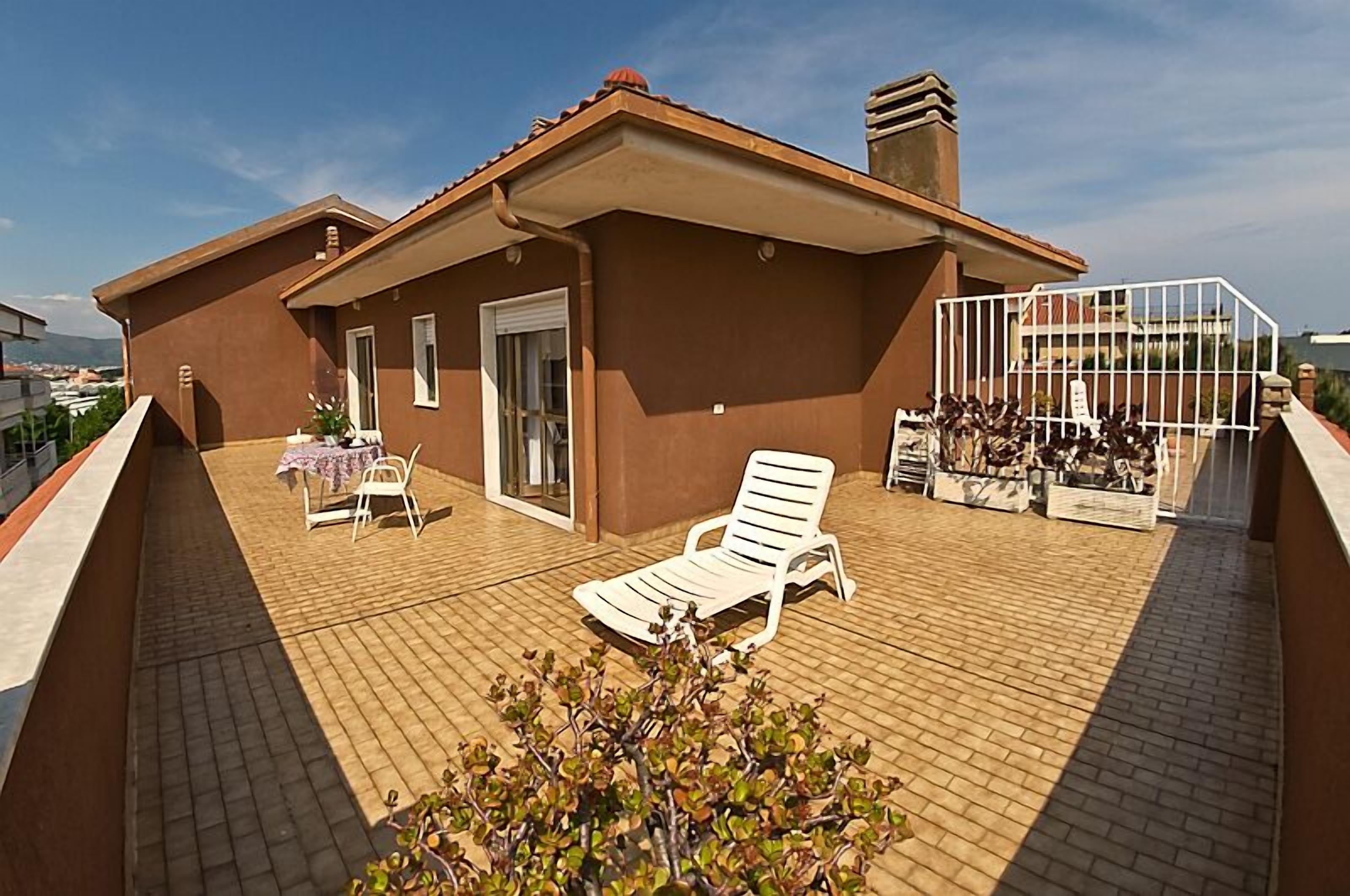 Eine Dachterrasse mit Liegestuhl, Tisch mit Tischdecke und weißem Zaun.