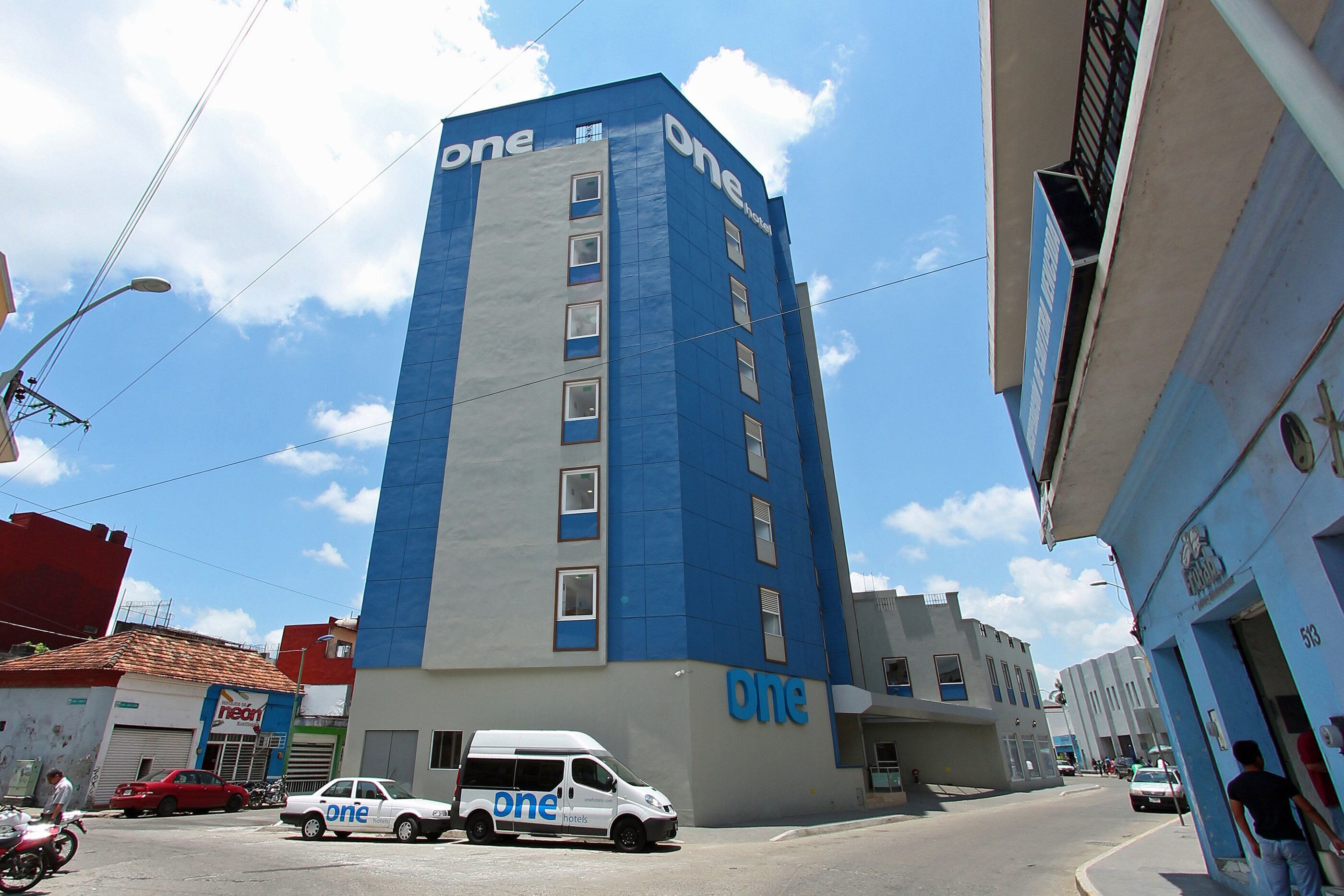 A tall building with a blue and white facade, multiple windows, and a sign indicating it is a hotel.