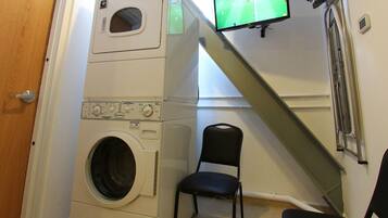 A laundry room with stacked washers and dryers, a TV mounted on the wall, and a chair.