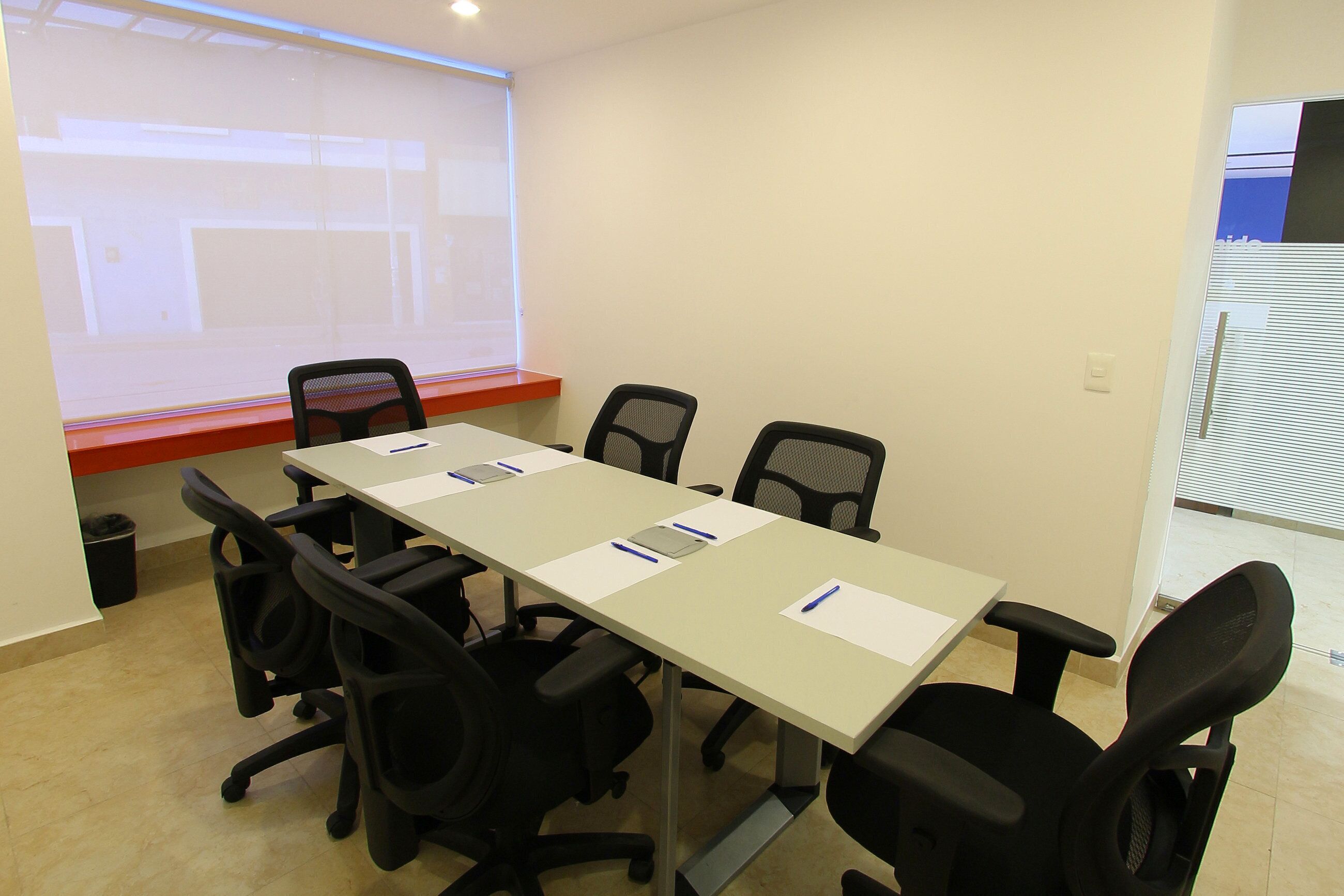 A conference room with a long table, six chairs, and a projector screen.