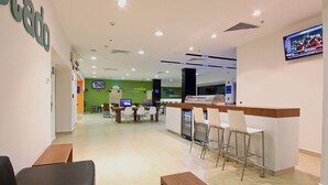 A modern hotel lobby with a reception desk, seating area, and a television screen. - One Villahermosa Centro (Villahermosa)