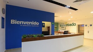 A reception desk with a blue wall and a sign that reads "Bienvenido te estamos esperando". - One Villahermosa Centro (Villahermosa)