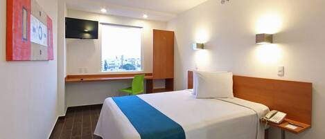 Quarto de hotel com cama, escrivaninha, cadeira, televisão e janela com vista para a cidade.