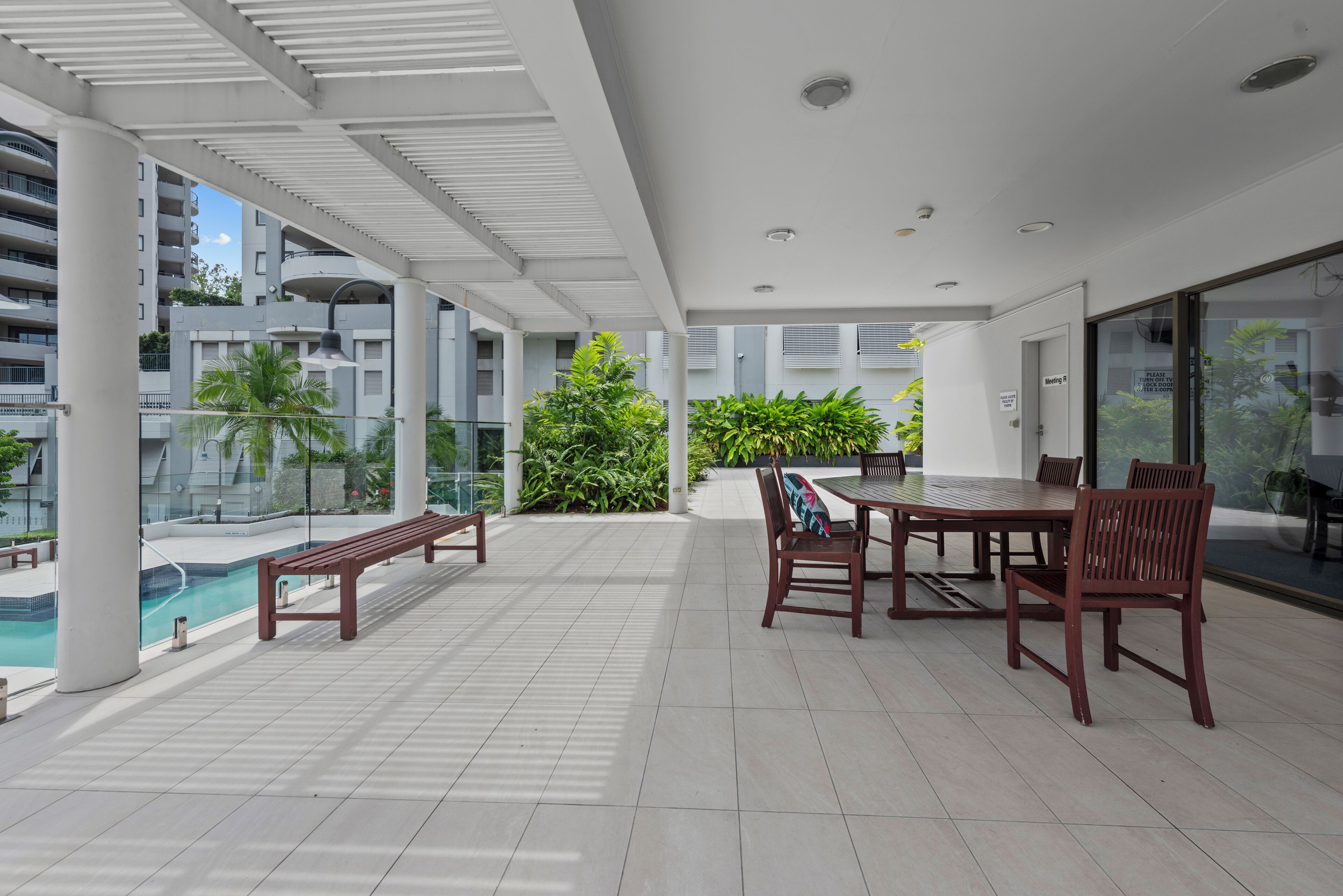 A spacious outdoor area with a pool, wooden benches, and a dining table with chairs.