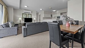 Quarto de hotel moderno com área de estar, mesa de jantar e cozinha compacta.