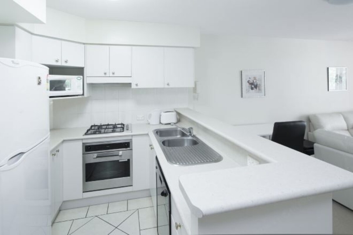A compact kitchen with white cabinets, a microwave, a stove, and a sink.