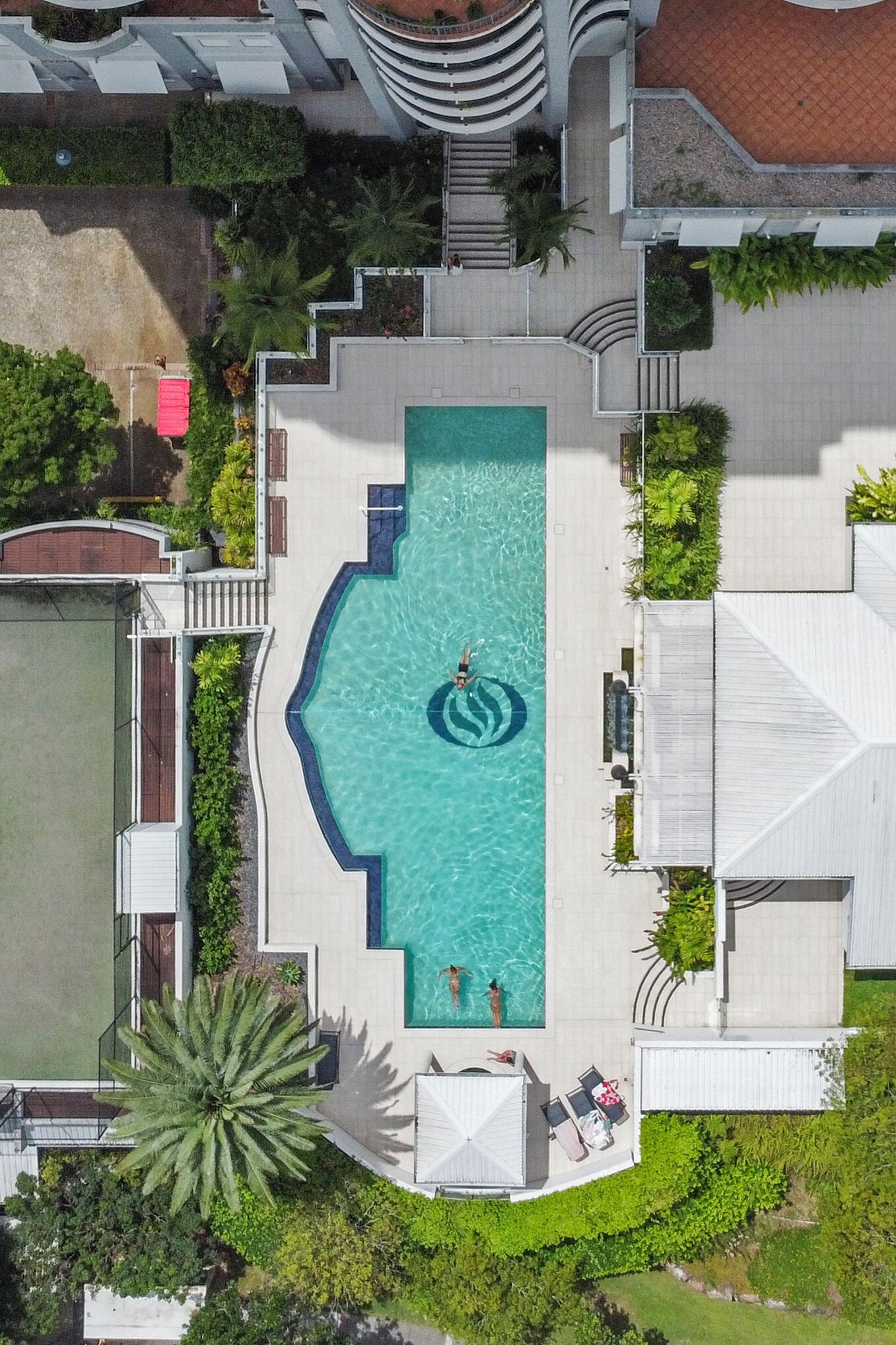 Ovenudblik over en ferieanlæg med en central swimmingpool, omgivet af frodig vegetation og moderne arkitektur.