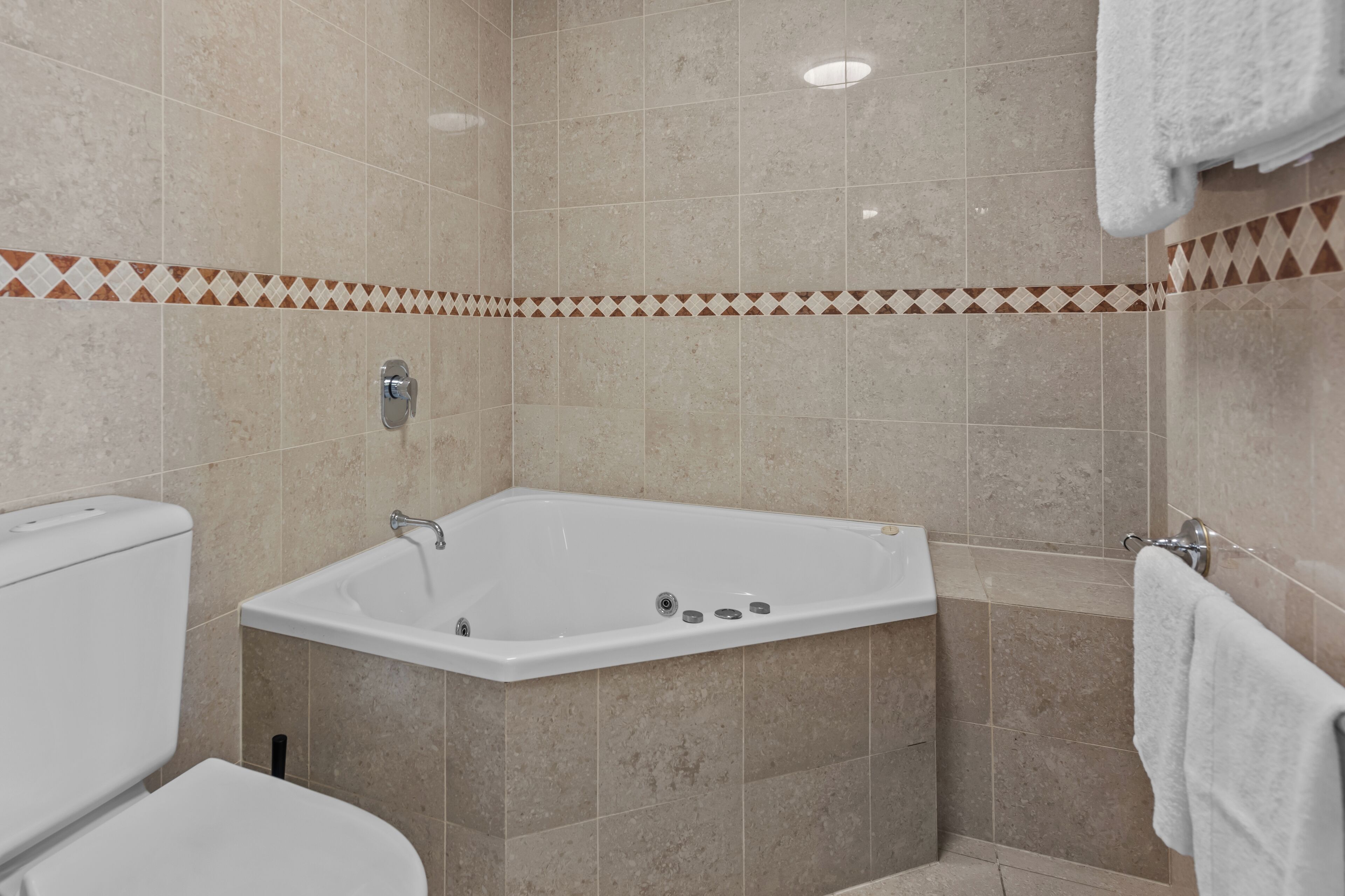 Un baño con bañera en esquina, inodoro y toallero.