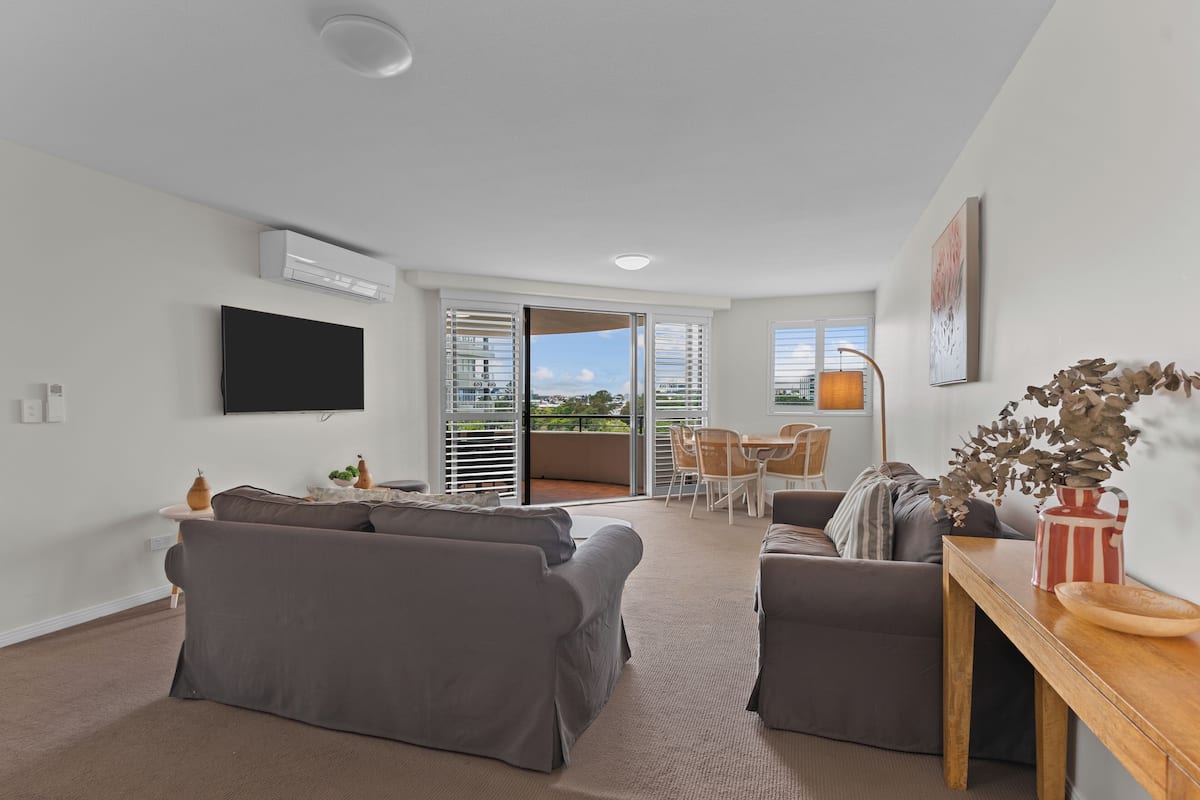 A modern living room with a grey sofa, a wooden coffee table, and a flat-screen TV mounted on the wall.