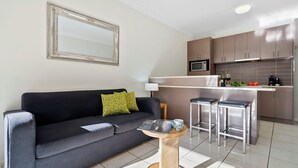 A modern living room with a sofa, a coffee table, and a kitchen area with cabinets and a microwave. - Emerald Inn by Travellers (Emerald)