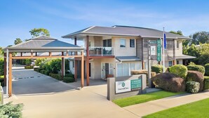 A modern hotel with a covered entrance, a signboard, and well-maintained landscaping. - Emerald Inn by Travellers (Emerald)
