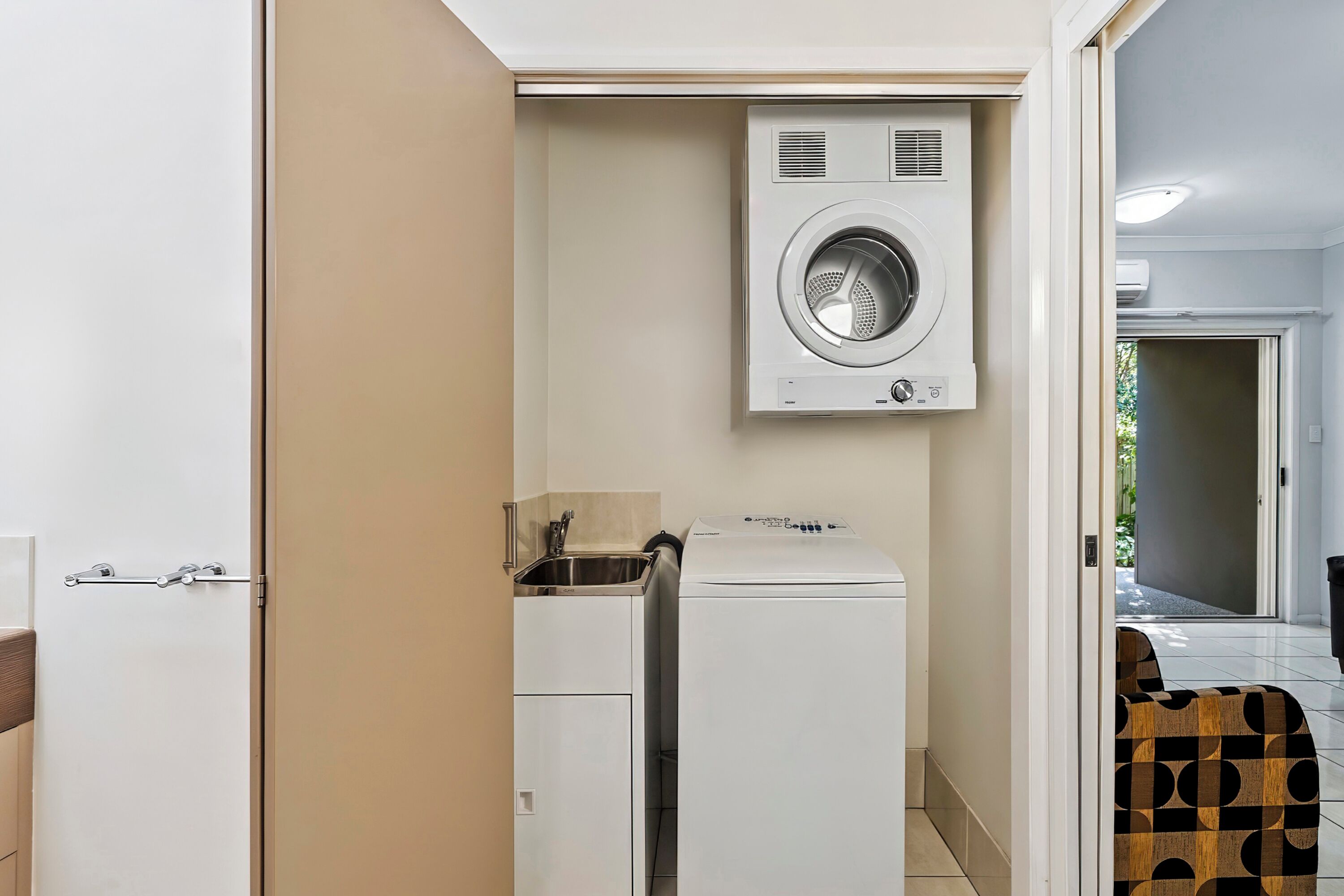A compact laundry room with a front-loading washer and dryer, a small sink, and a door leading to another room.