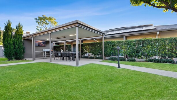A modern building with a covered patio area, a well-maintained lawn, and a hedge. - Emerald Inn by Travellers (Emerald)