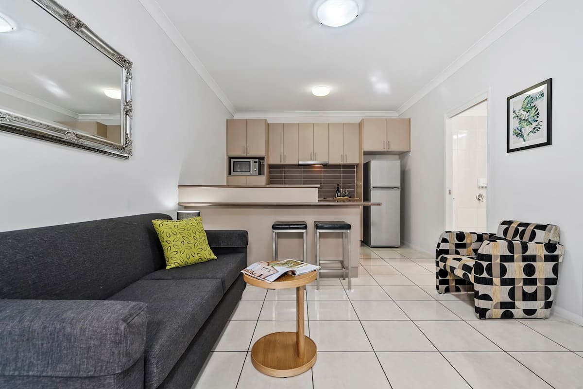 A modern living room with a grey sofa, a small wooden side table, and a black and white patterned sofa.