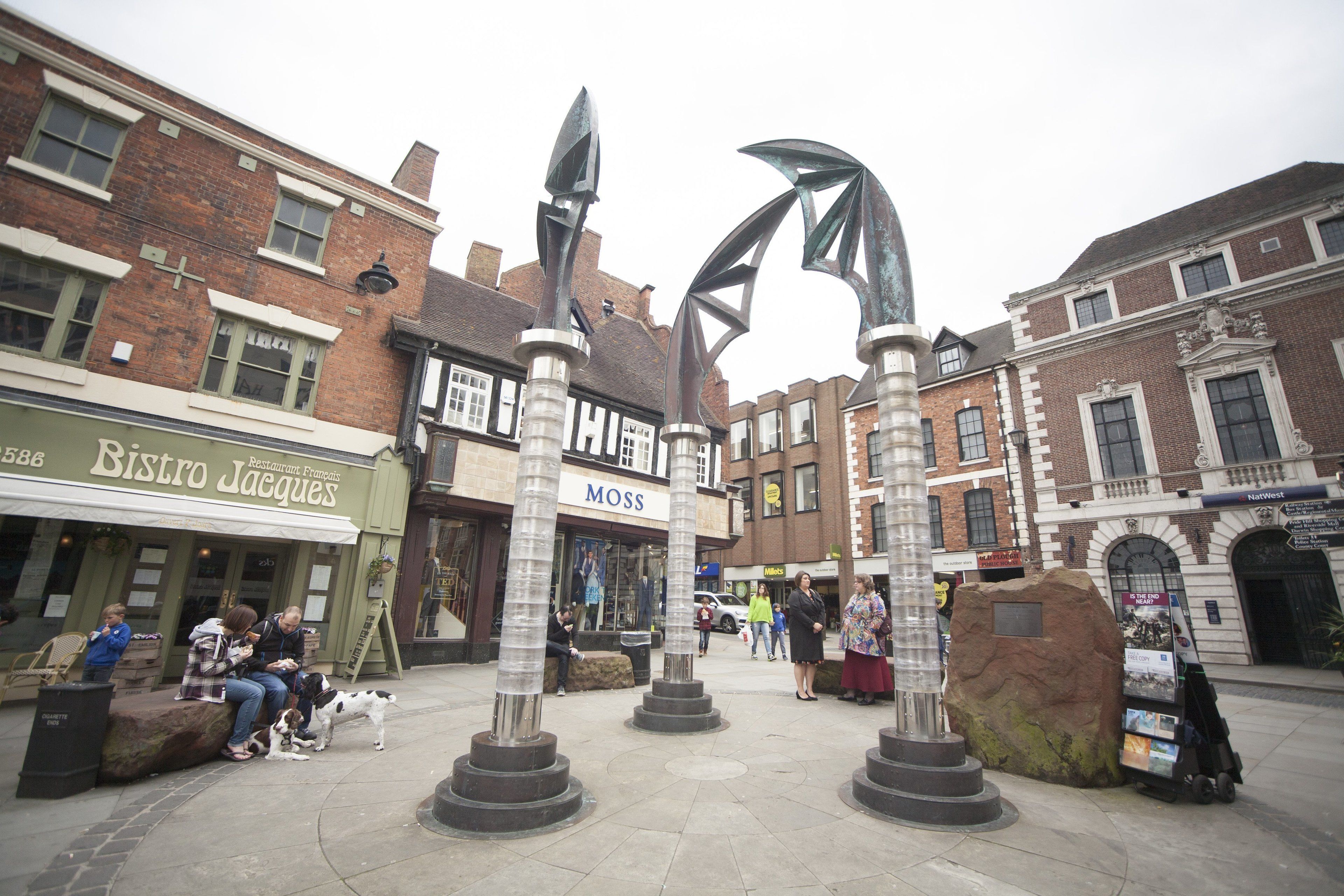 A public square with a bistro, a Moss store, and a large rock sculpture.