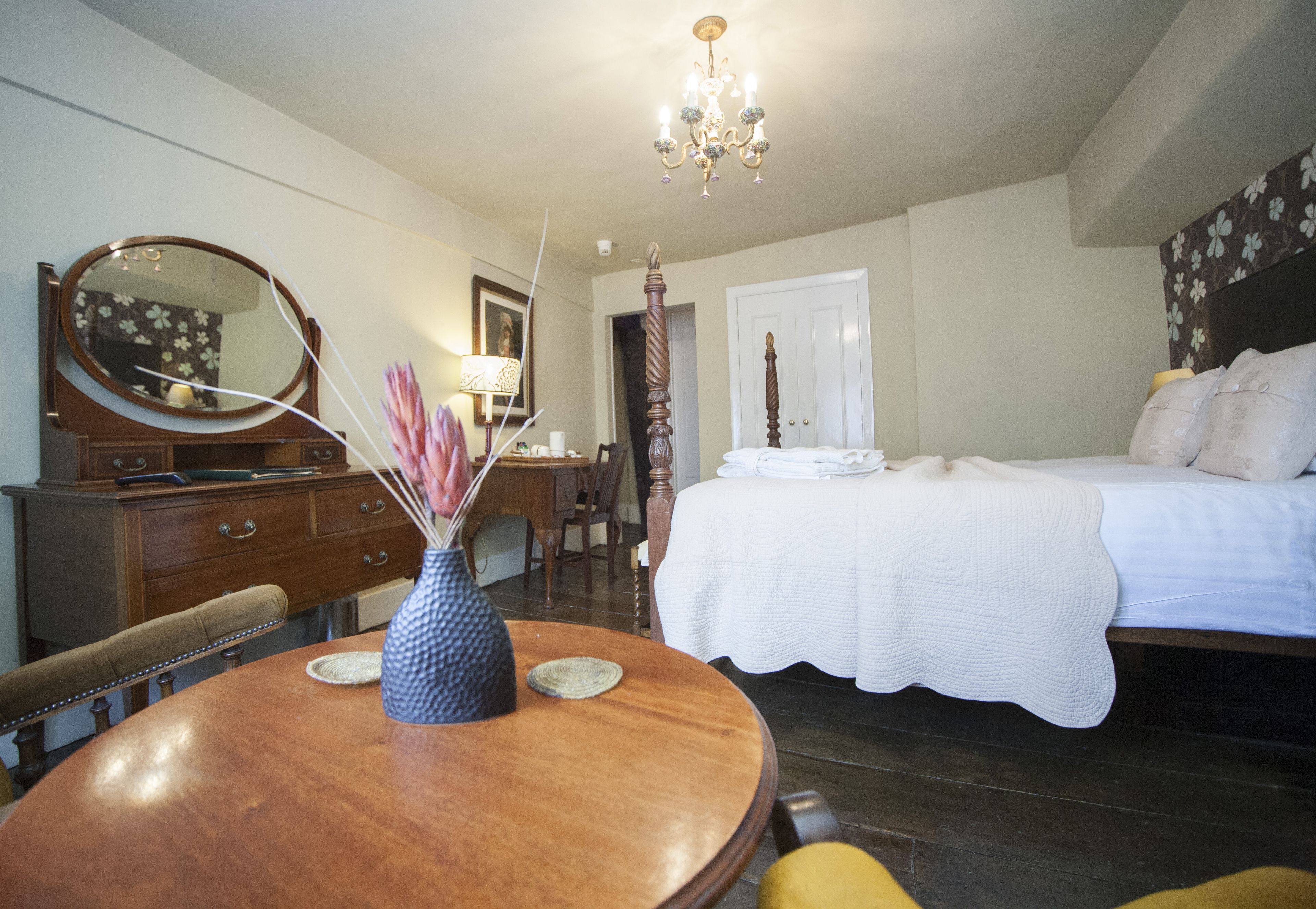A bedroom with a bed, a dresser, a mirror, a chandelier, and a dining table with chairs.