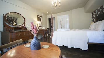 A bedroom with a bed, a dresser, a mirror, a chandelier, and a dining table with chairs.