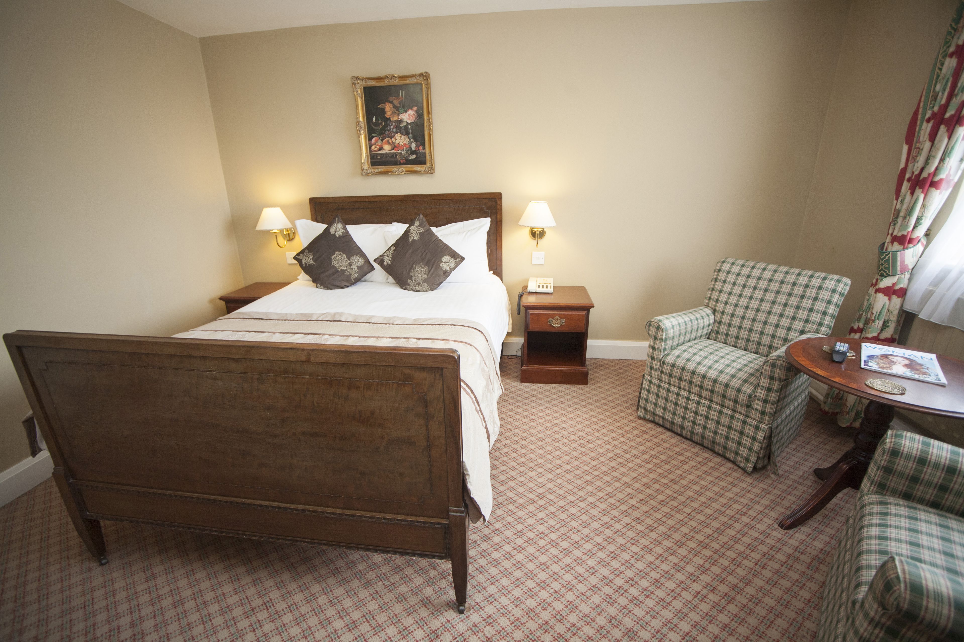 Une chambre d’hôtel avec un lit en bois, deux tables de chevet avec des lampes, une chaise et une petite table sur laquelle se trouve un livre.