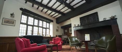 A room with a high ceiling, exposed beams, a fireplace, and a patterned carpet.