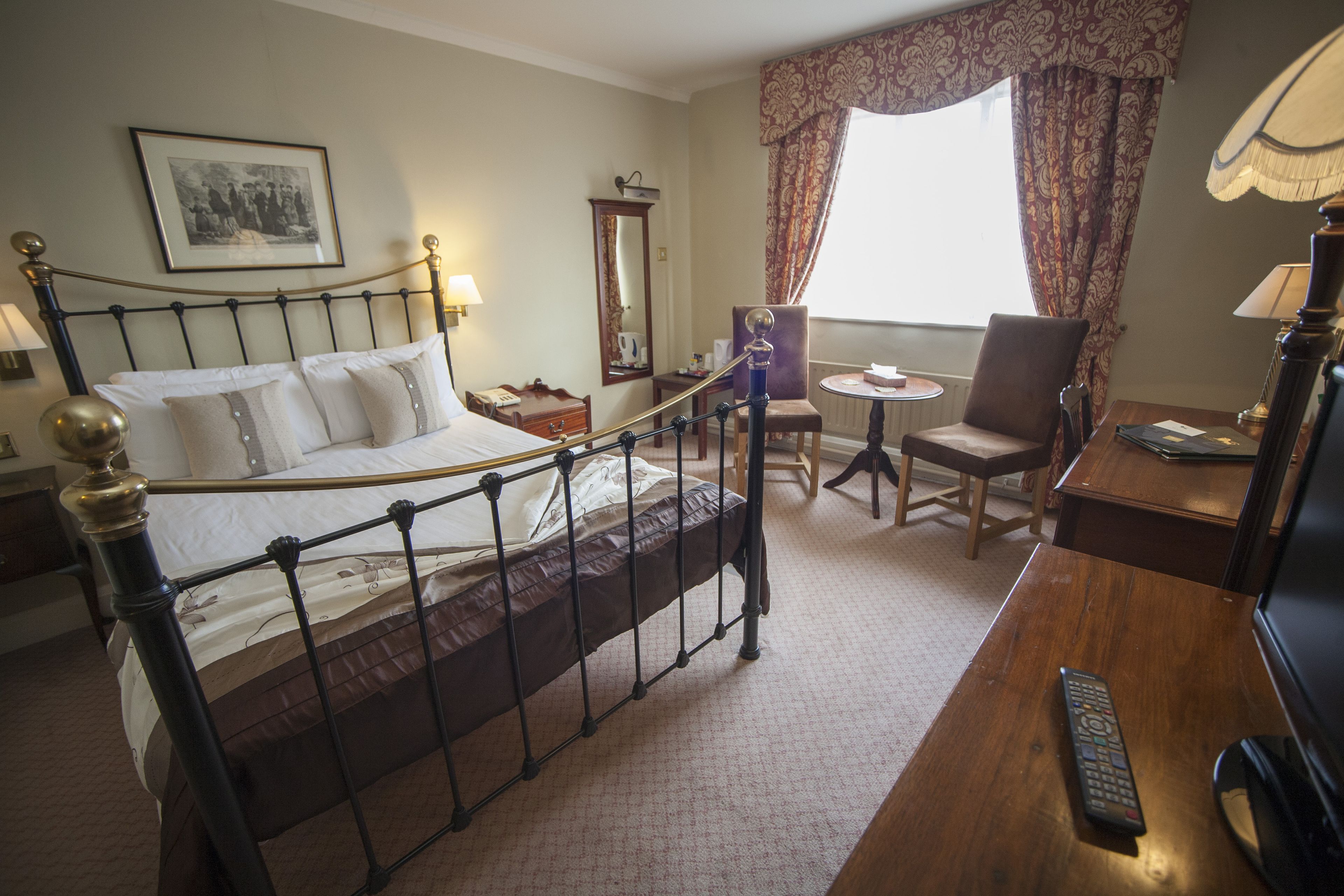 A hotel room with a bed, a desk, a chair, a lamp, and a window with curtains.