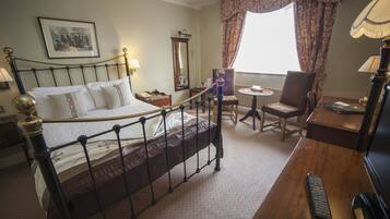 A hotel room with a bed, a desk, a chair, a lamp, and a window with curtains.