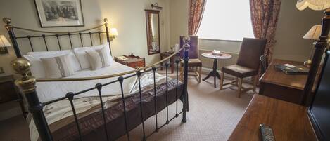 A hotel room with a bed, a desk, a chair, a lamp, and a window with curtains.