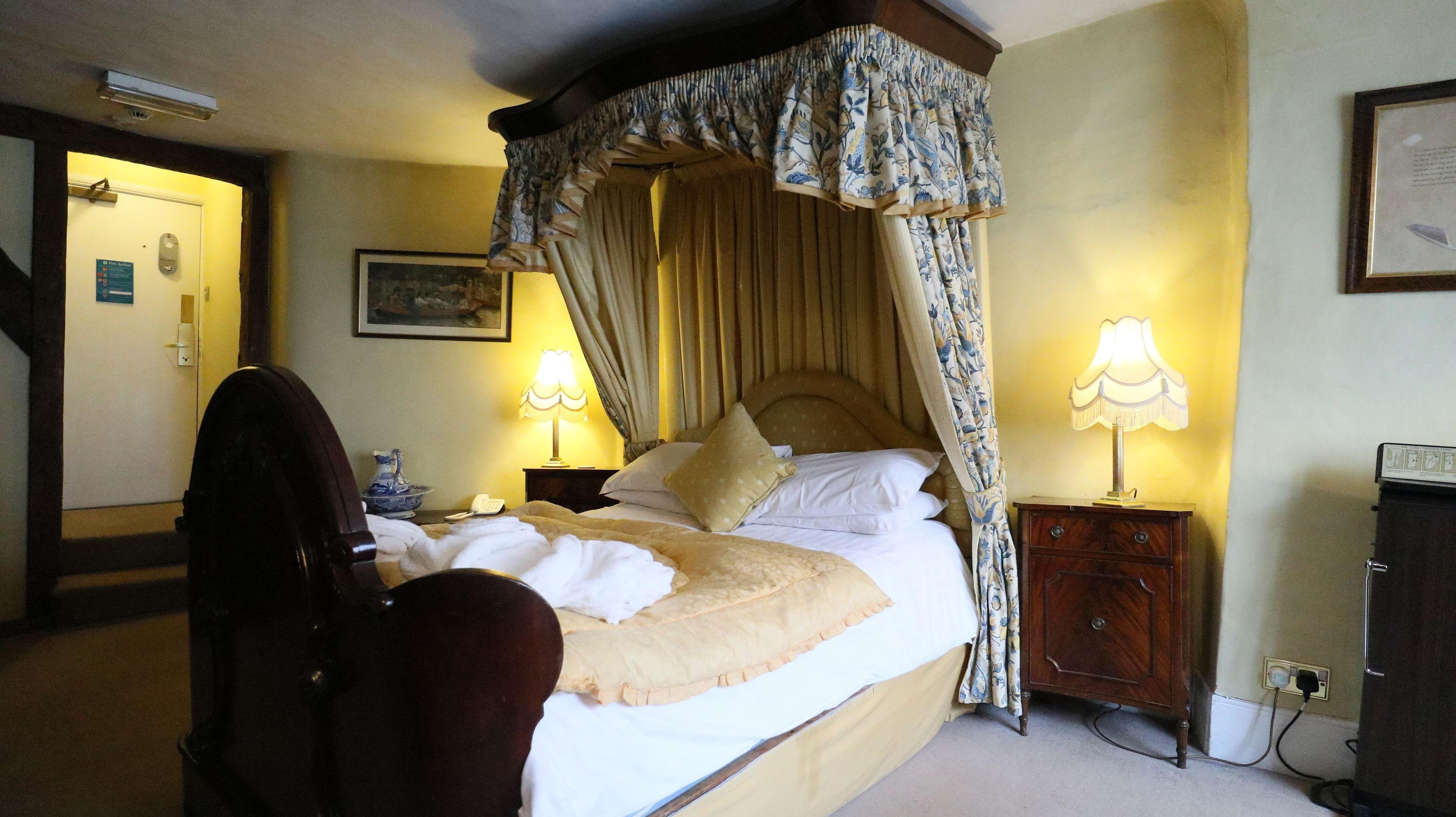 A four-poster canopy bed with a headboard, two bedside lamps, a bedside telephone, and a wooden nightstand.