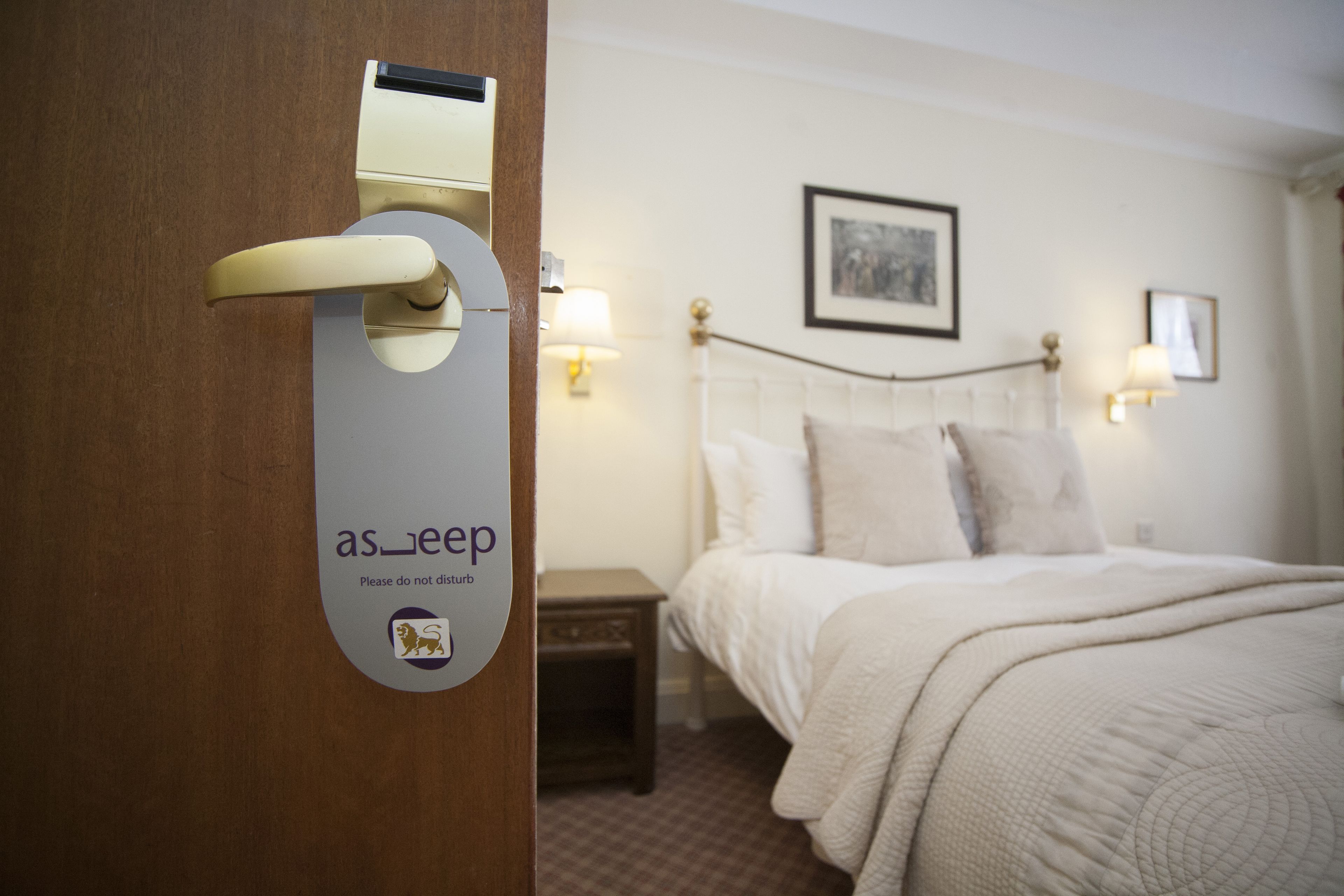 Une chambre d’hôtel avec un lit, des lampes de chevet, une table de nuit et une porte avec une pancarte.
