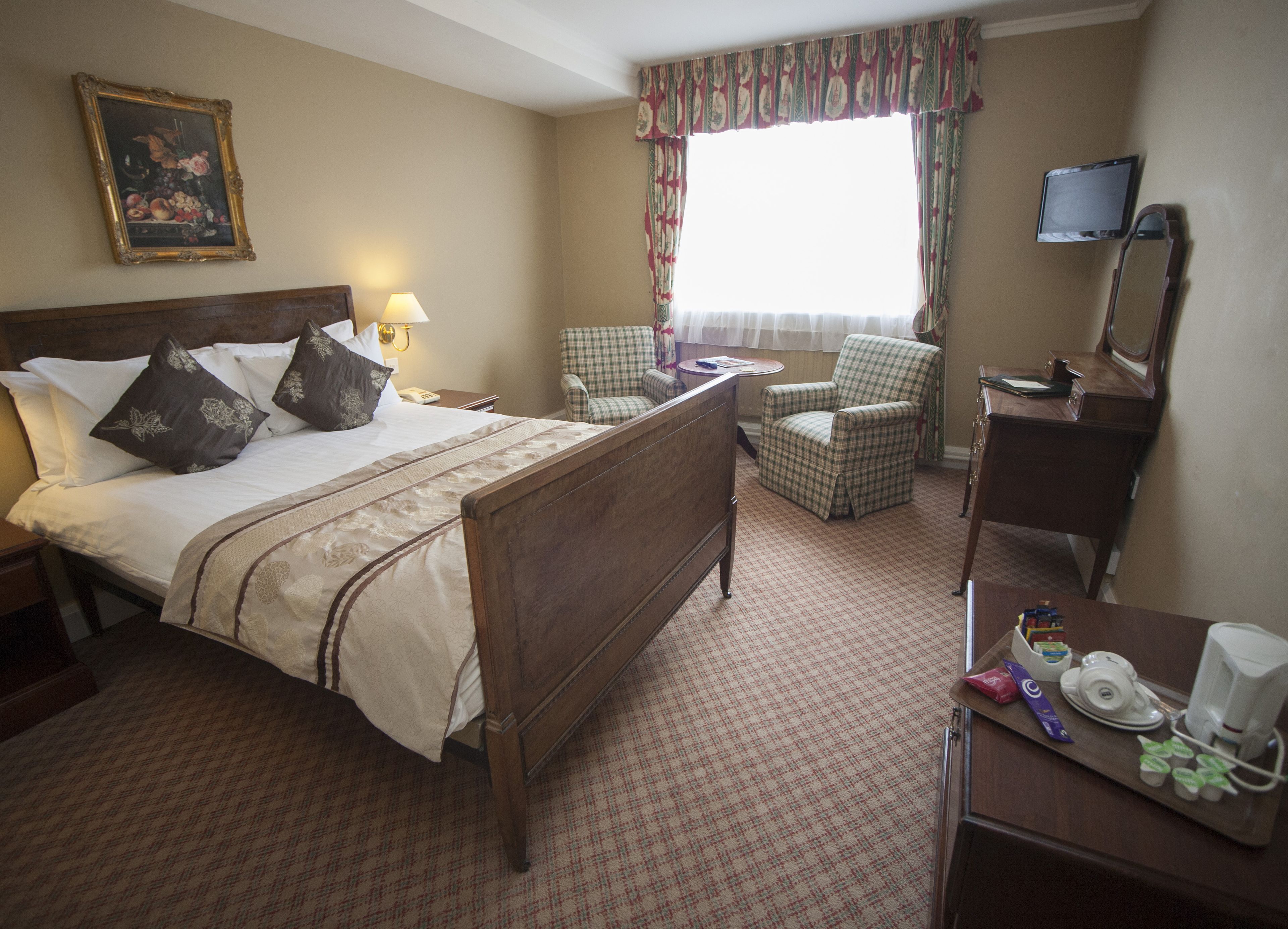 A hotel room with a large bed, a desk with a mirror, a chair, a television, and a painting on the wall.