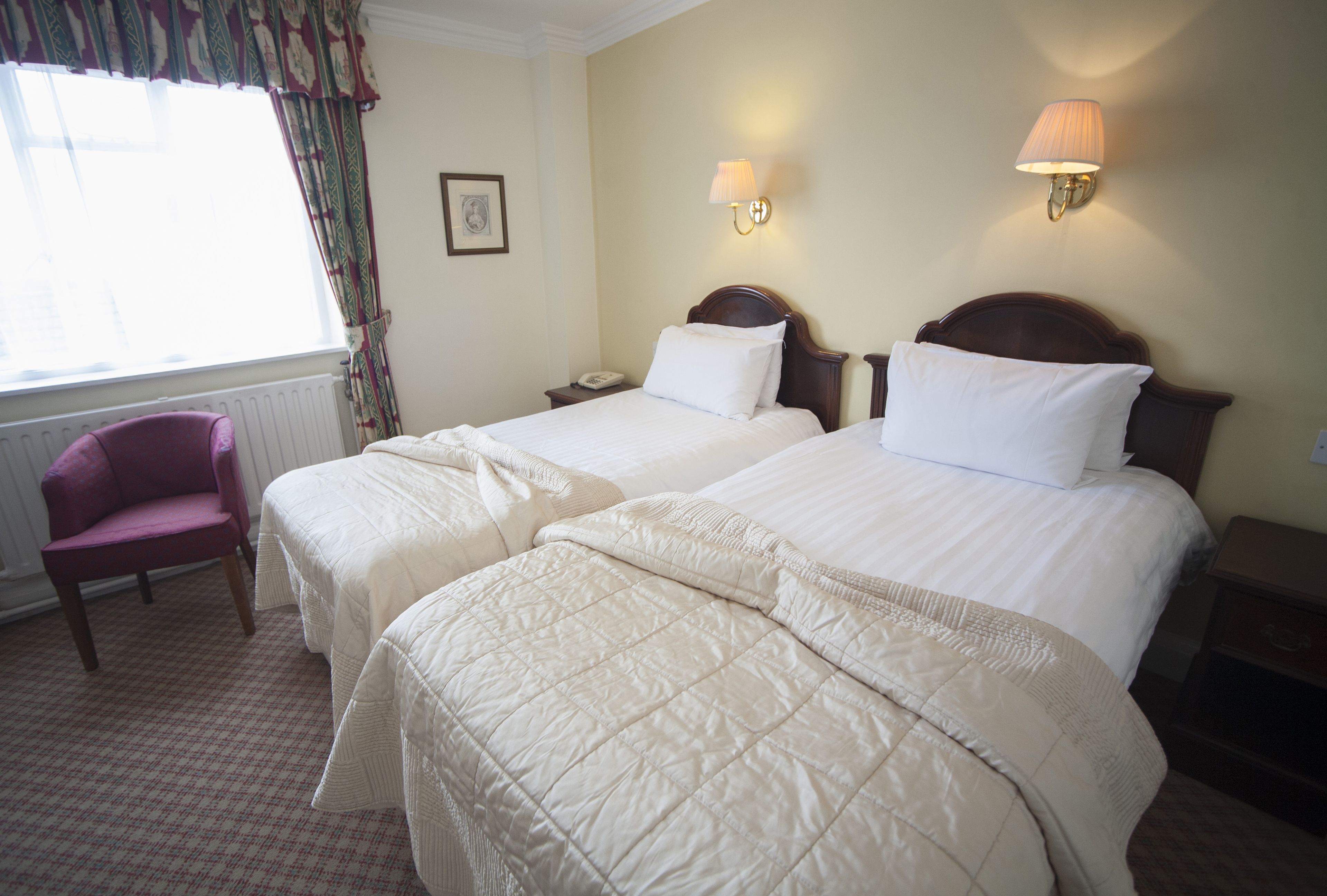 Une chambre d’hôtel avec deux lits, une chaise et une table de chevet avec une lampe.