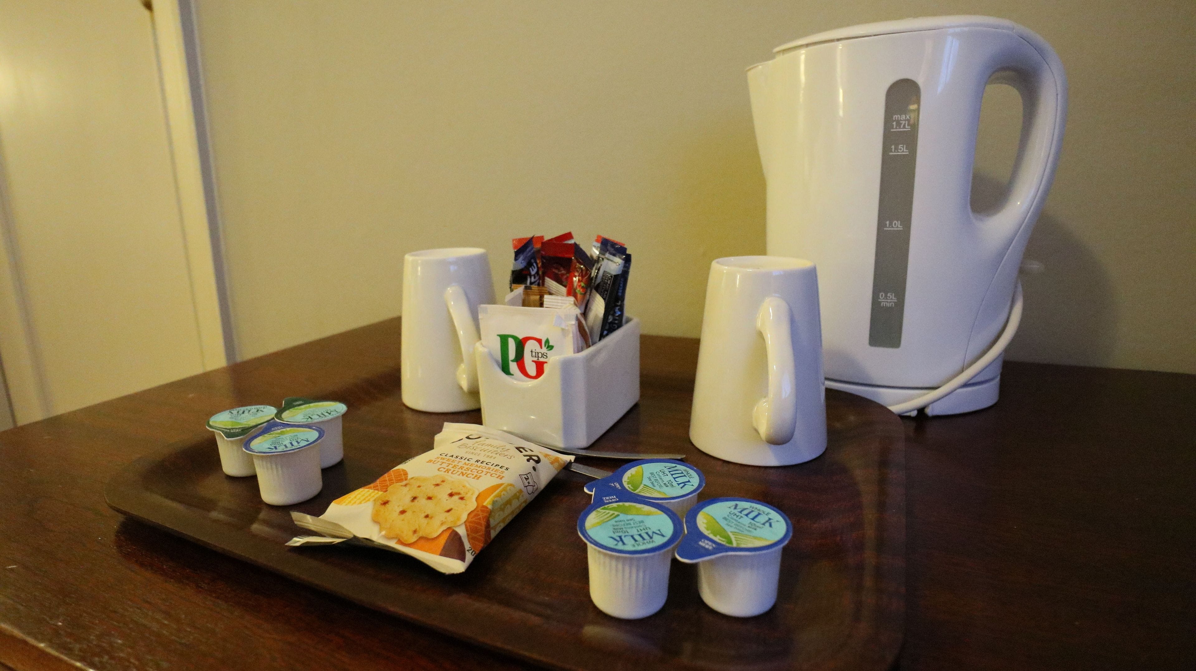 A breakfast setup with a coffee maker, a mug, a container with PG tips, and several yogurt cups.