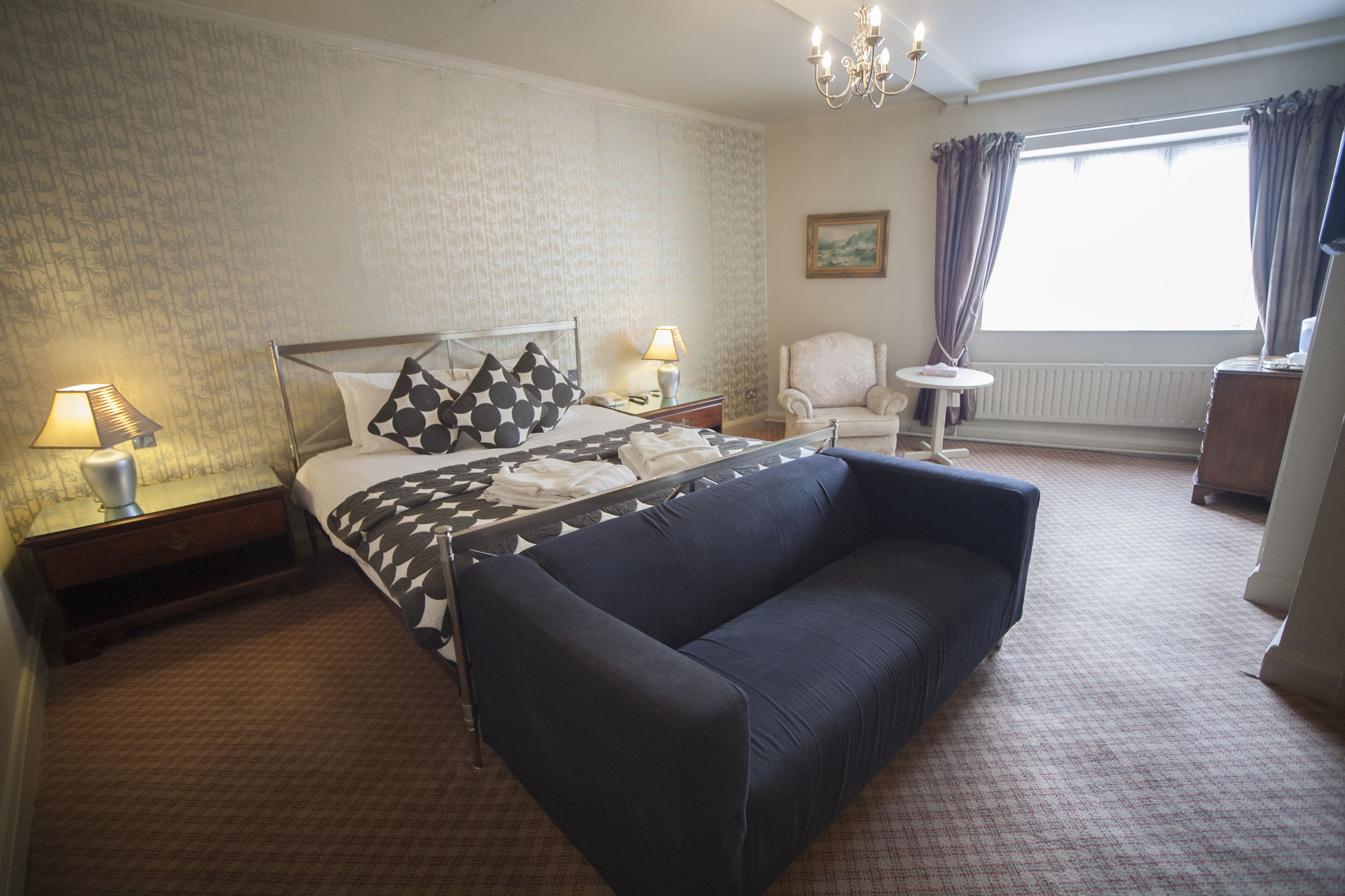 Una habitación de hotel con cama, sofá, sillón, mesita y ventana con cortinas.