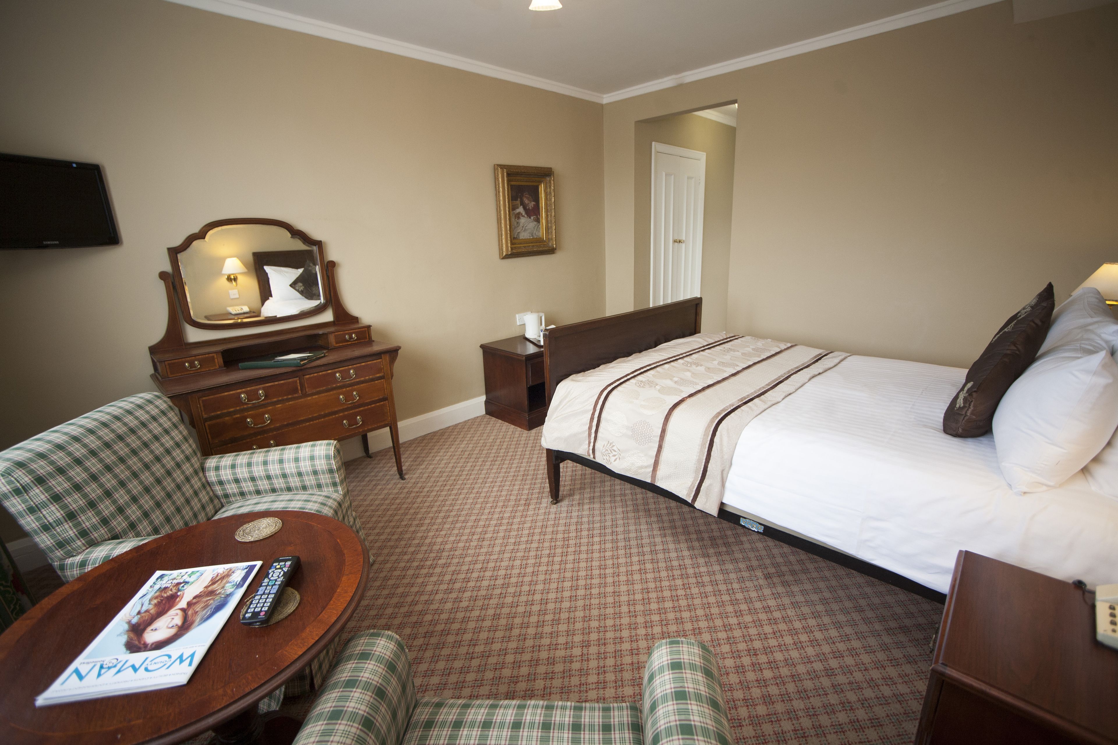A hotel room with a bed, a desk, a chair, a dresser, and a television.