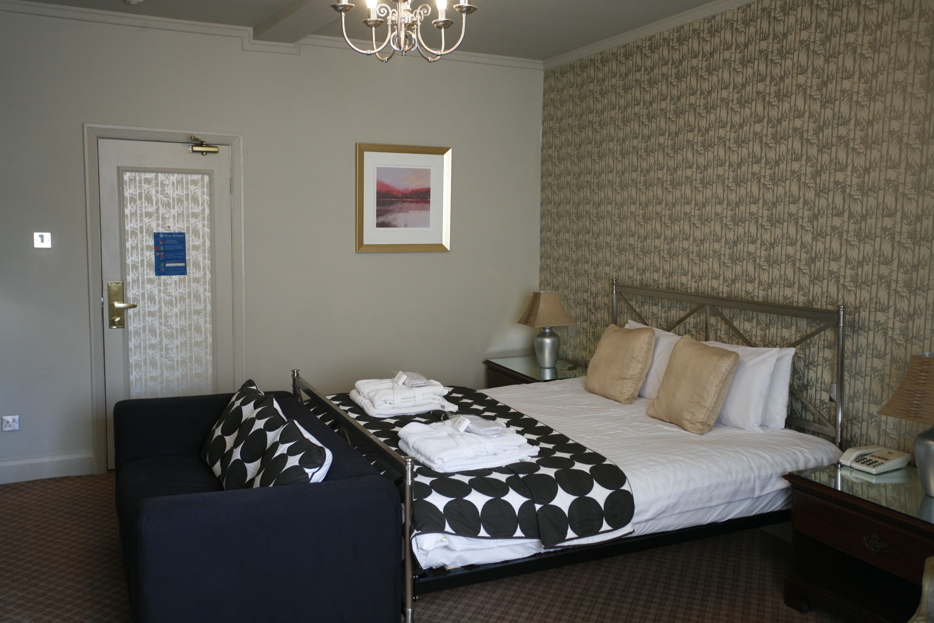 Une chambre d’hôtel avec un lit, une chaise, une table de chevet, une lampe et une porte avec une pancarte.