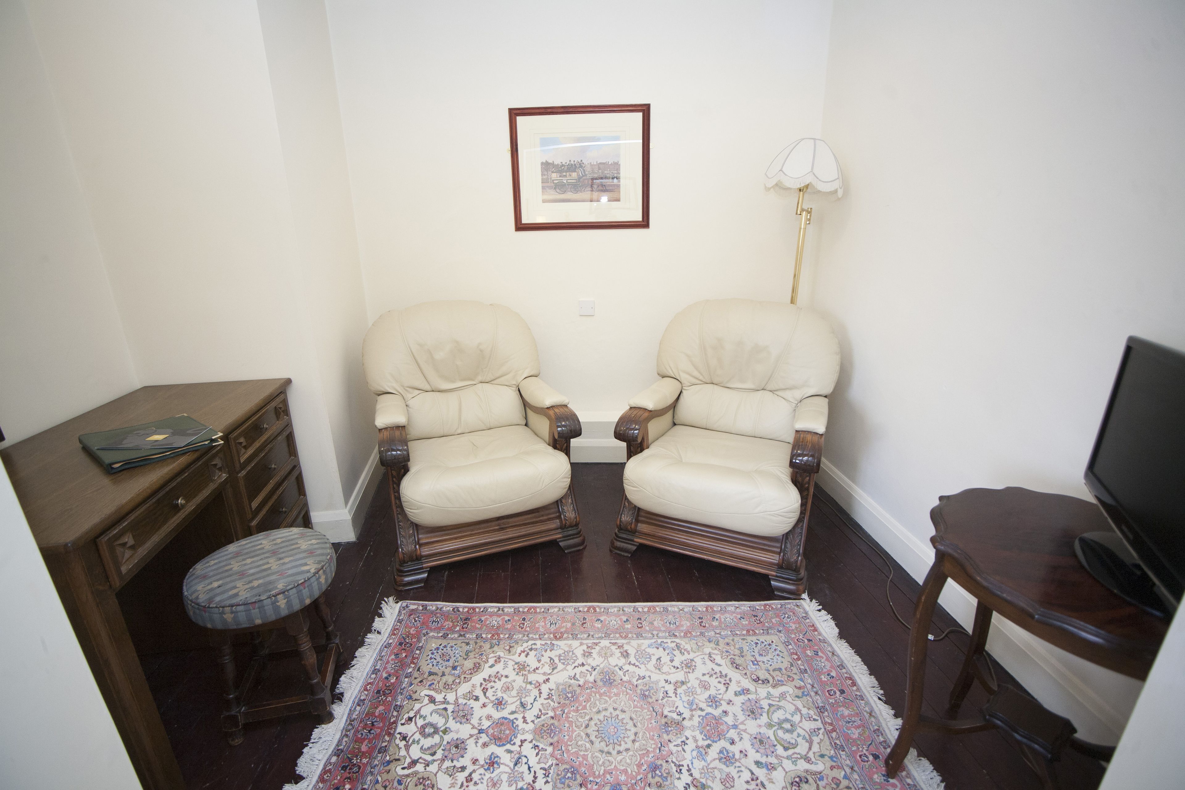 A room with two armchairs, a small table, a television, a lamp, and a framed picture on the wall.