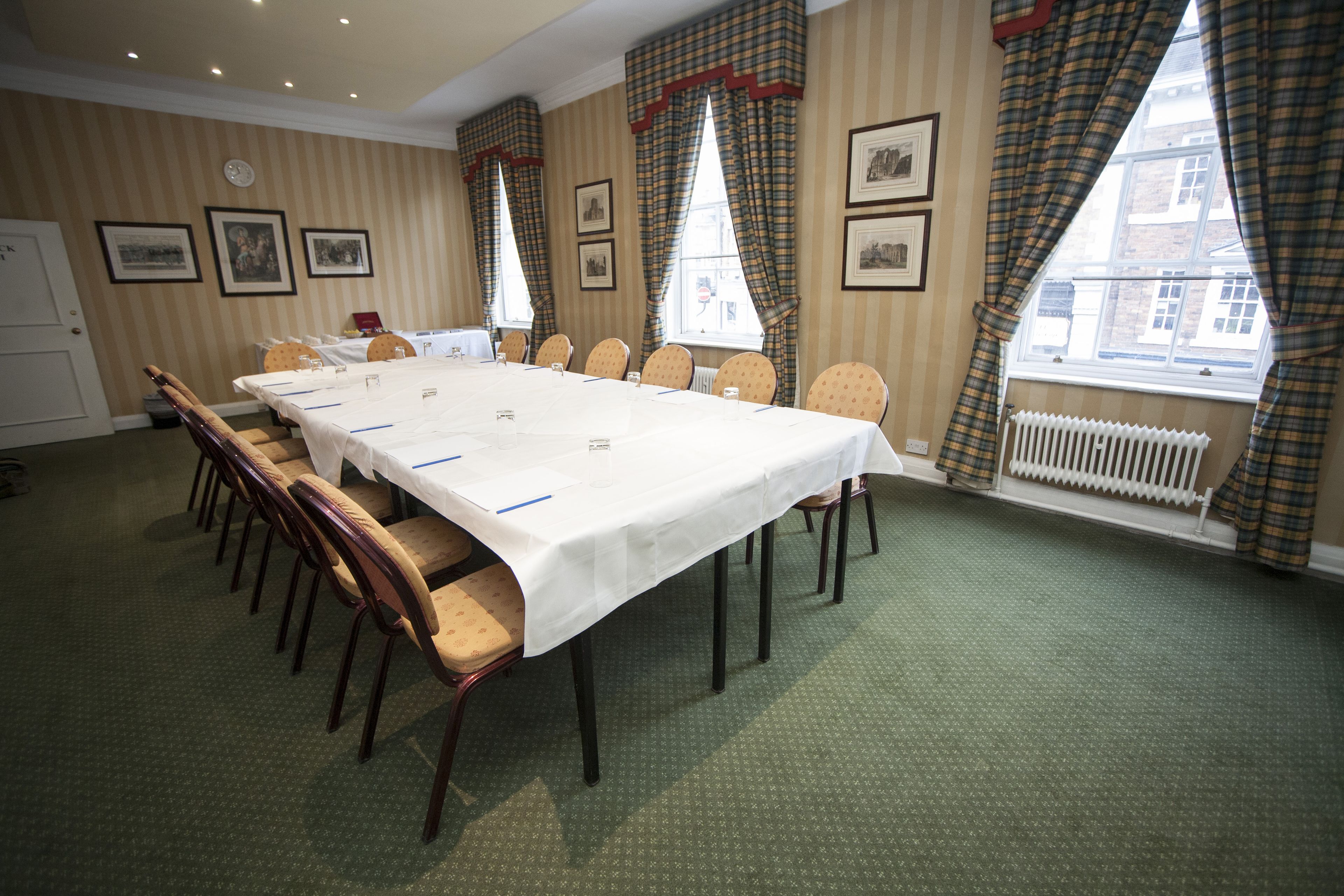 A conference room with a long table, chairs, framed pictures on the walls, and a window with curtains.