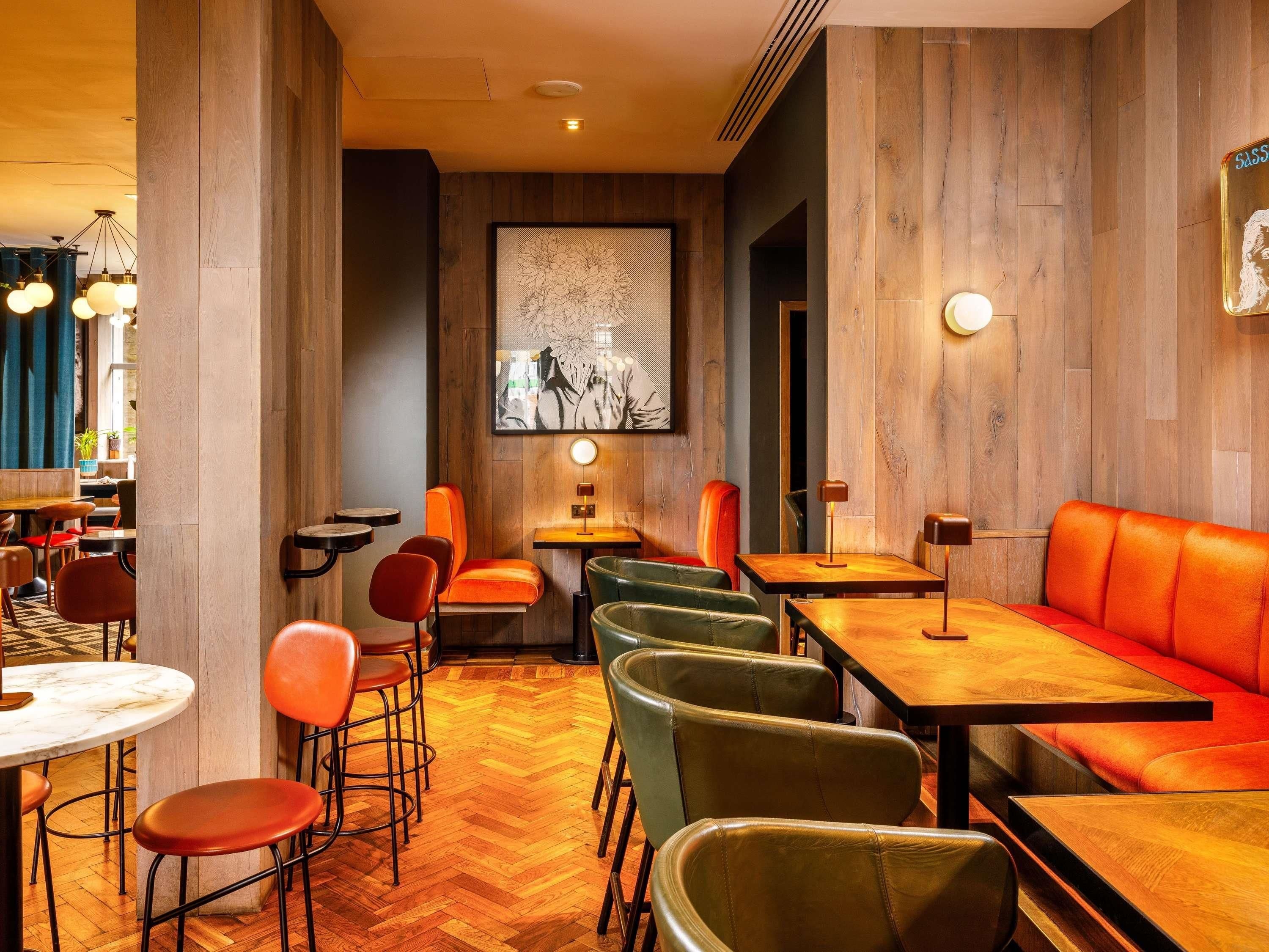 A restaurant interior with wooden panel walls, a large floral artwork, and a mix of red and green upholstered seating.