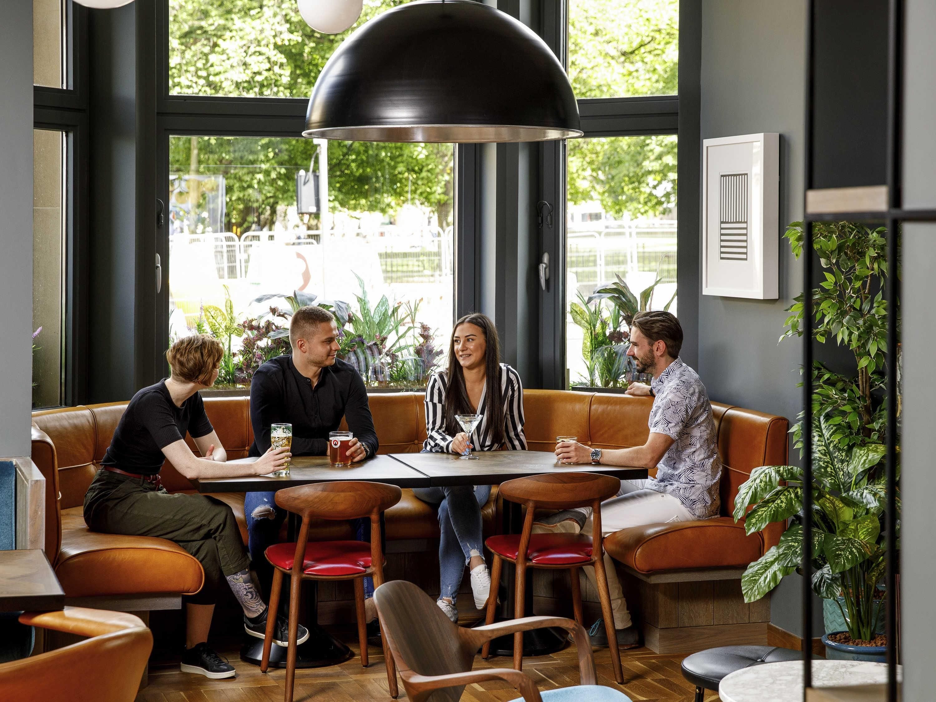 Un grupo de personas sentadas en una mesa en un café moderno con ventanas amplias y plantas de interior.
