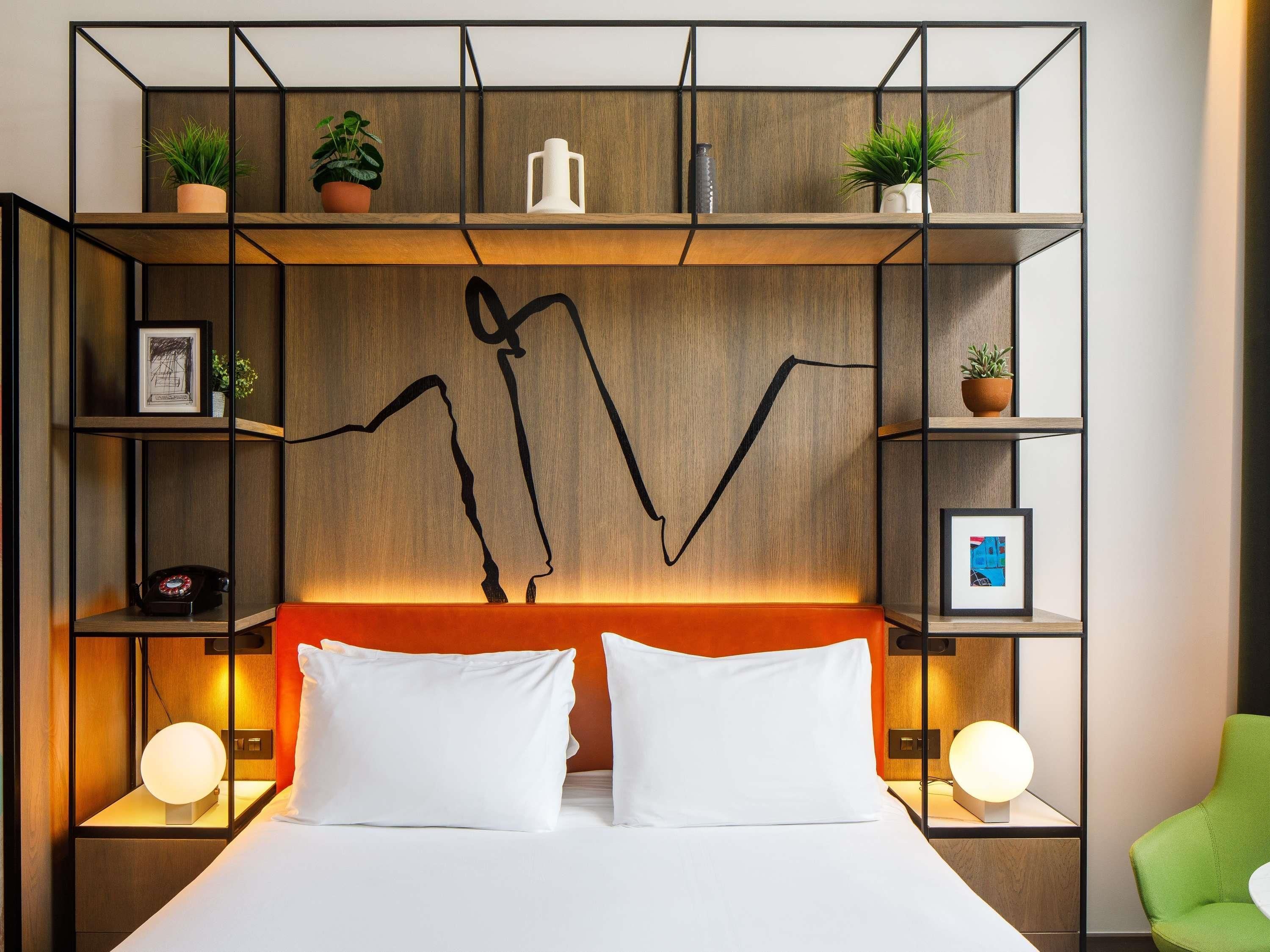 Habitación de hotel con cama, dos lámparas de noche, una obra de arte abstracta en la pared y una silla verde.