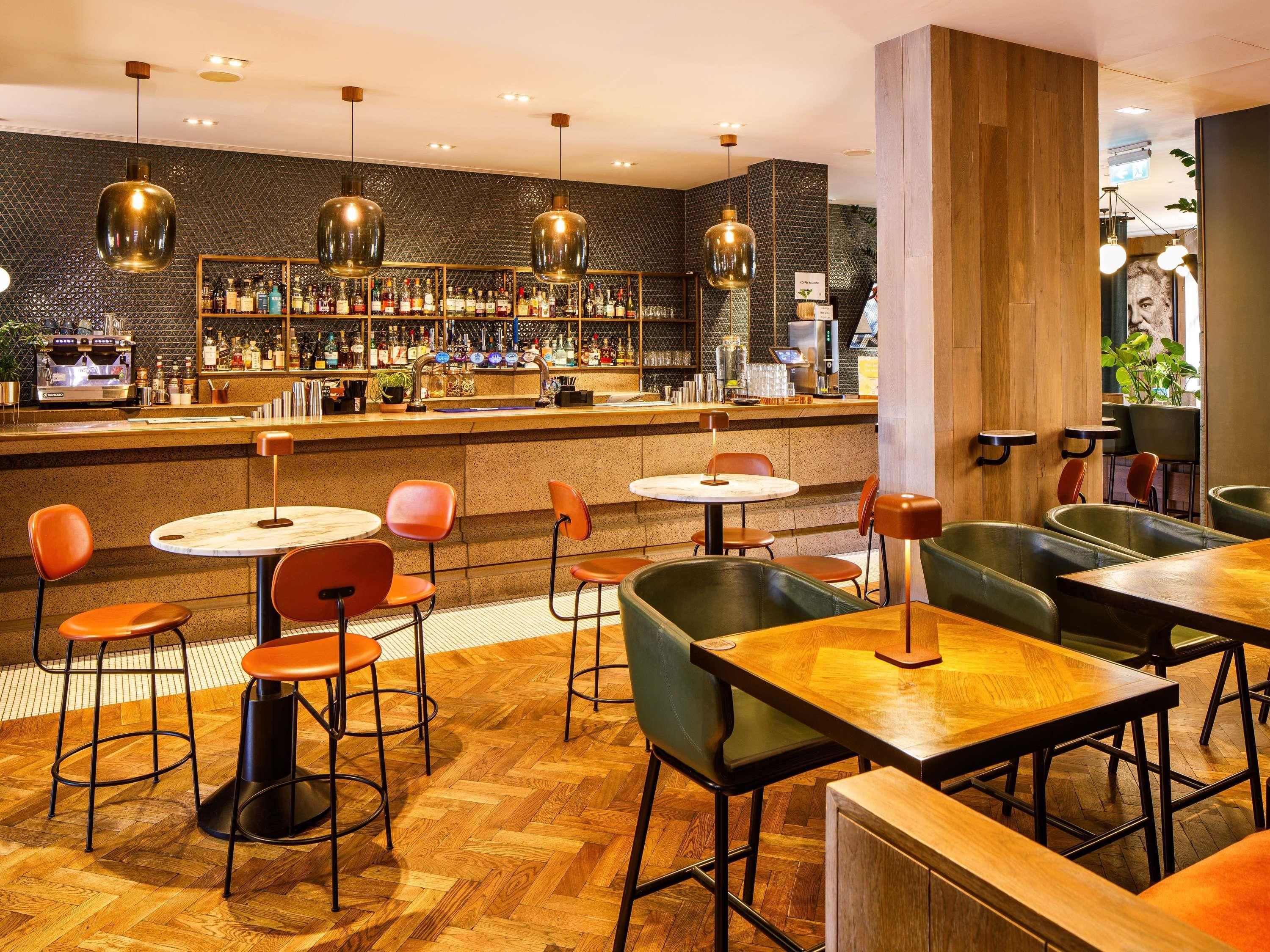 A bar area with multiple seating options, including round tables and booths, and a bar counter with a variety of bottles and a coffee machine.