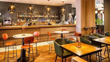 A bar area with multiple seating options, including round tables and booths, and a bar counter with a variety of bottles and a coffee machine.
