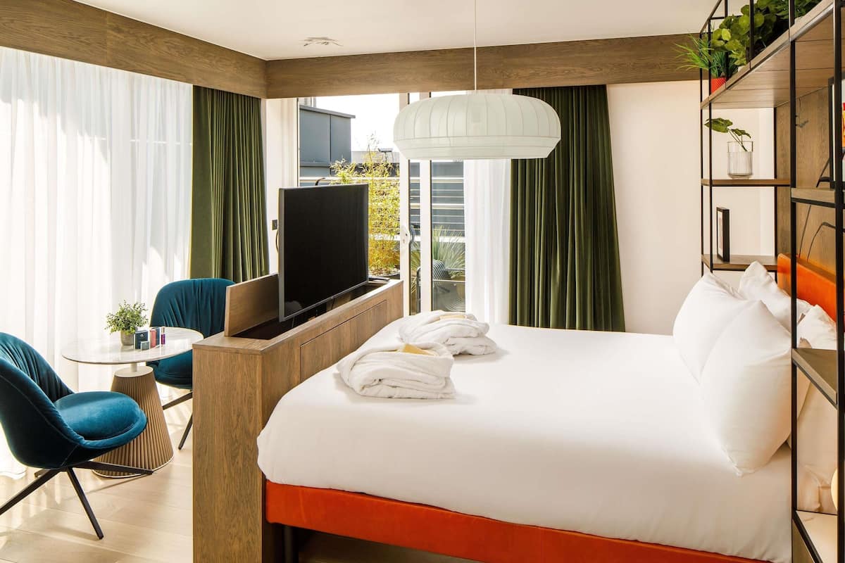 Une chambre d’hôtel avec un lit, un bureau, une chaise, une télévision et une fenêtre avec des rideaux.