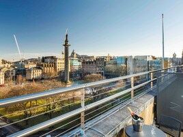 A balcony with a view of a cityscape, including historic and modern buildings, a statue, and a distant tower.