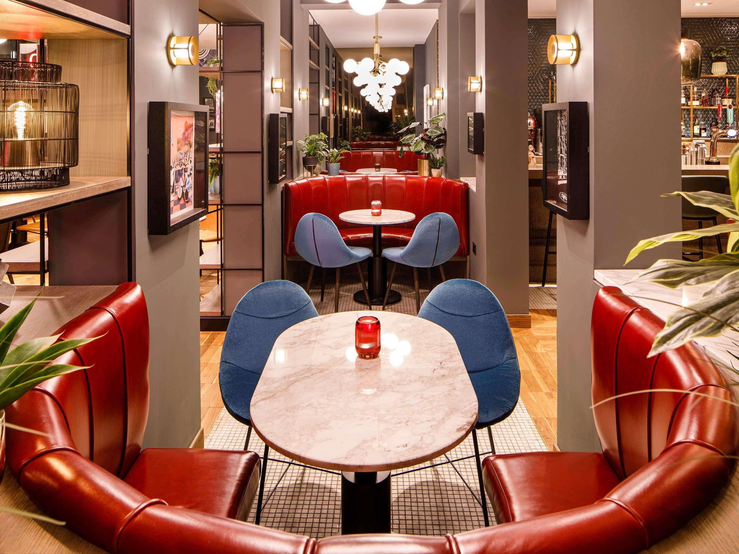 A modern interior with red leather booths, blue chairs, and a marble table.
