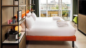 A modern hotel room with a large bed, a balcony with a view of the city, and a small table with chairs. - ibis Styles Edinburgh Centre St Andrew Square (Edinburgh)