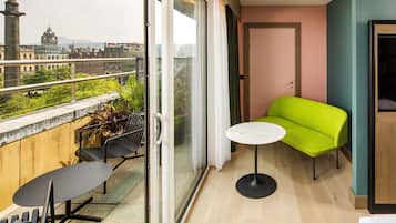 Un balcón con mesa y sillas, un sofá verde y vistas a edificios.