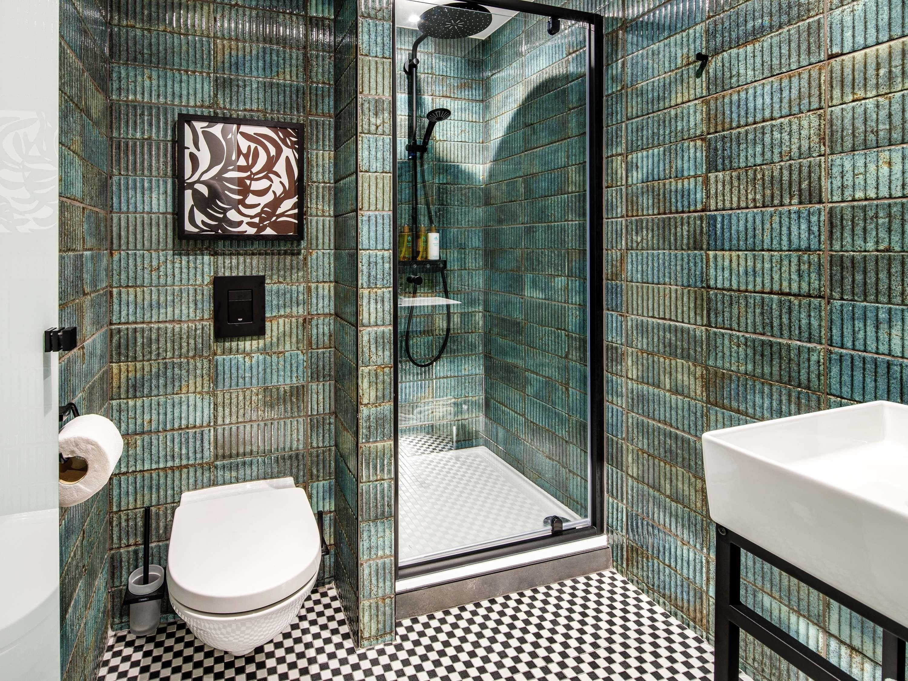 A bathroom with a checkered floor, a white toilet, a glass shower enclosure, and a sink.
