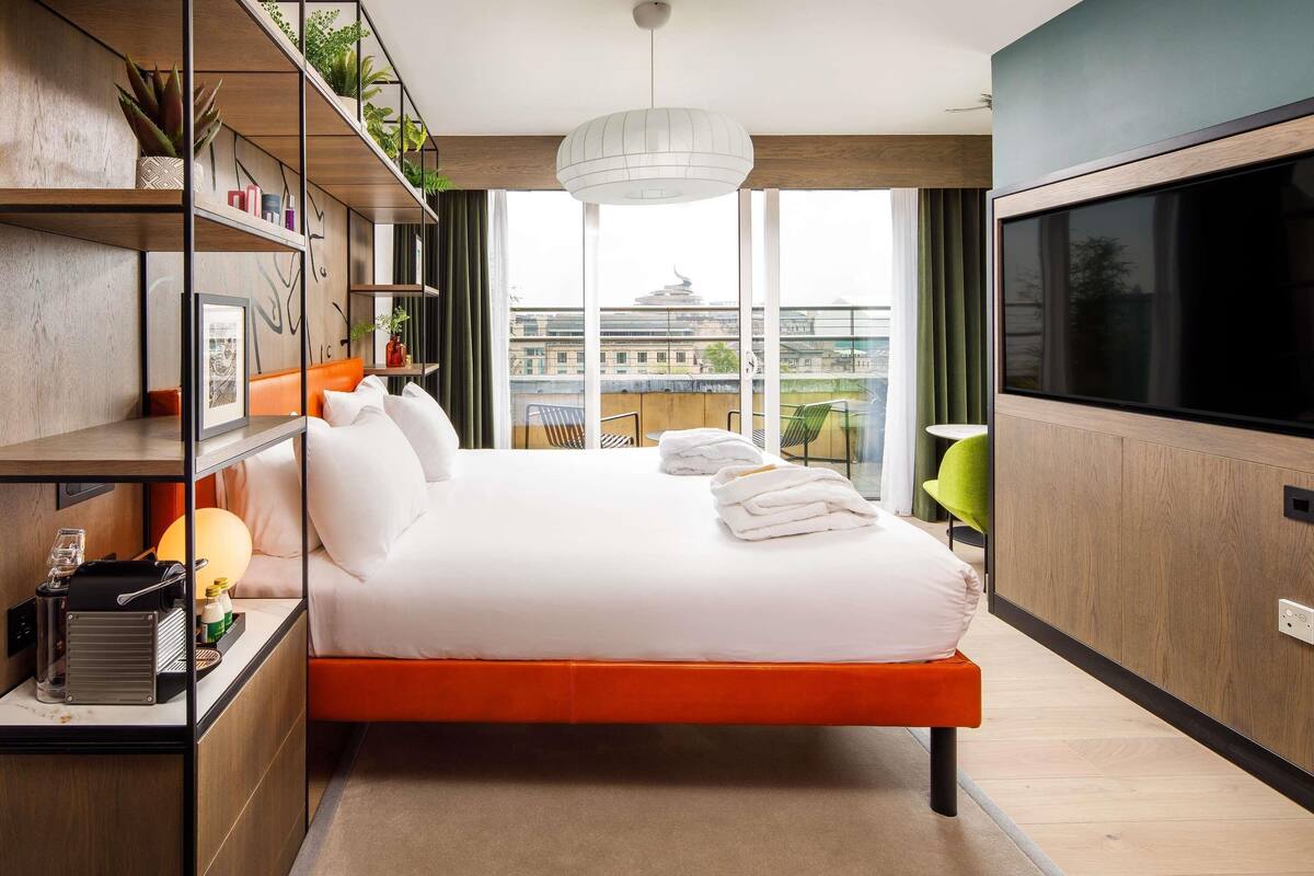 Une chambre d’hôtel moderne avec un grand lit, une télévision, une bibliothèque et une vue sur la ville.