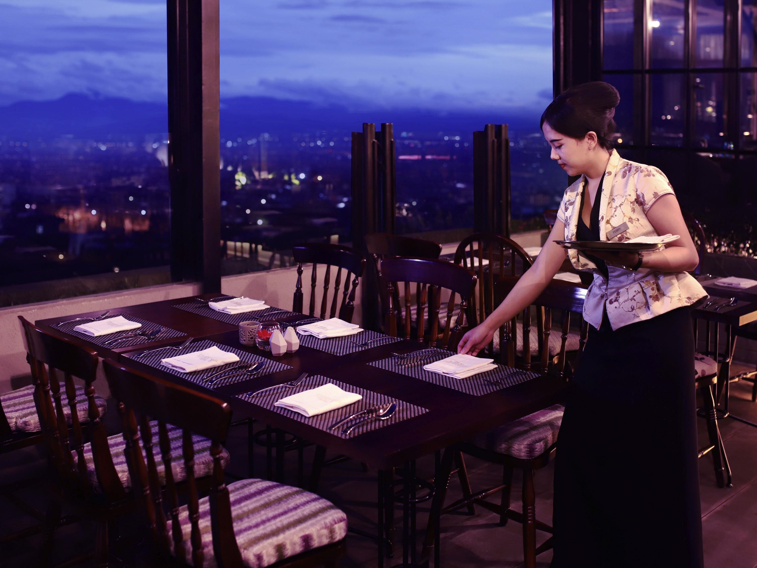 A dining area with a table set for four, chairs, and a view of a cityscape through large windows.