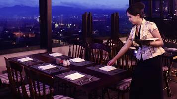 A dining area with a table set for four, chairs, and a view of a cityscape through large windows.